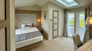 A bedroom with a bed, bedside table, lamp, and a view through a window. - Platinum 2 Bed Spa Slps 4 (Pet) (Clarach)