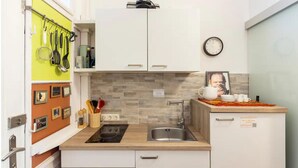 A compact kitchen with white cabinets, a built-in stove, a sink, and a clock on the wall.