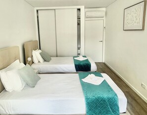 A hotel room with two beds, a wardrobe, a door, and a wall-mounted air conditioning unit. - Luxury T3 Plaza Inn | A/C, Lift, Balcony in Town Centre (Funchal)