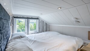 A bedroom with a sloped ceiling, a large bed, a window, and a wall-mounted light fixture. - Aura Chalet (Pet Friendly) (Coldstream)