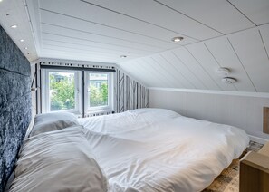 Un dormitorio con techo inclinado, una cama grande, una ventana y un aplique de pared.