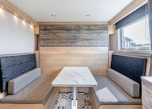 Un interior acogedor con una mesa central, dos zonas de estar con cojines y una ventana con vistas.