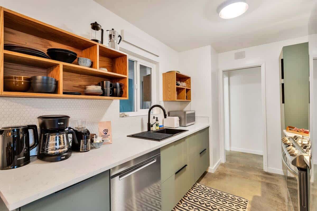 A modern kitchen with wooden shelves, a coffee maker, a microwave, and a sink.