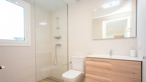 Un baño moderno con cabina de ducha de vidrio, inodoro blanco y tocador de madera con espejo.