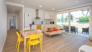 Una cocina moderna con gabinetes blancos, extractor de acero inoxidable y un comedor con mesa de vidrio y sillas amarillas.