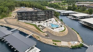 A multi-story hotel with a pool, surrounded by water and greenery. - Vintage Villa - Luxury Condo, Infinity Pool, & Gym! (Village of Four Seasons)