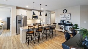 A modern kitchen with white cabinets, stainless steel appliances, and a central island with bar stools. - Vintage Villa - Luxury Condo, Infinity Pool, & Gym! (Village of Four Seasons)