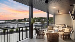 A covered outdoor seating area with wicker furniture, a view of a waterfront, and a sunset. - Vintage Villa - Luxury Condo, Infinity Pool, & Gym! (Village of Four Seasons)