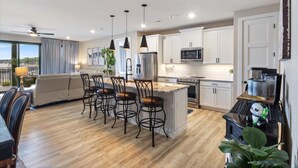 A modern kitchen with white cabinets, a central island with bar stools, and a dining area with a sofa and chairs. - Vintage Villa - Luxury Condo, Infinity Pool, & Gym! (Village of Four Seasons)