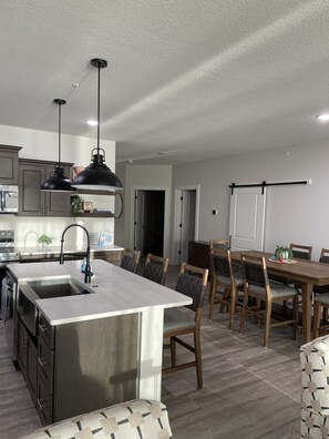 A modern kitchen with a central island, stainless steel appliances, and a dining area with wooden chairs and a table.
