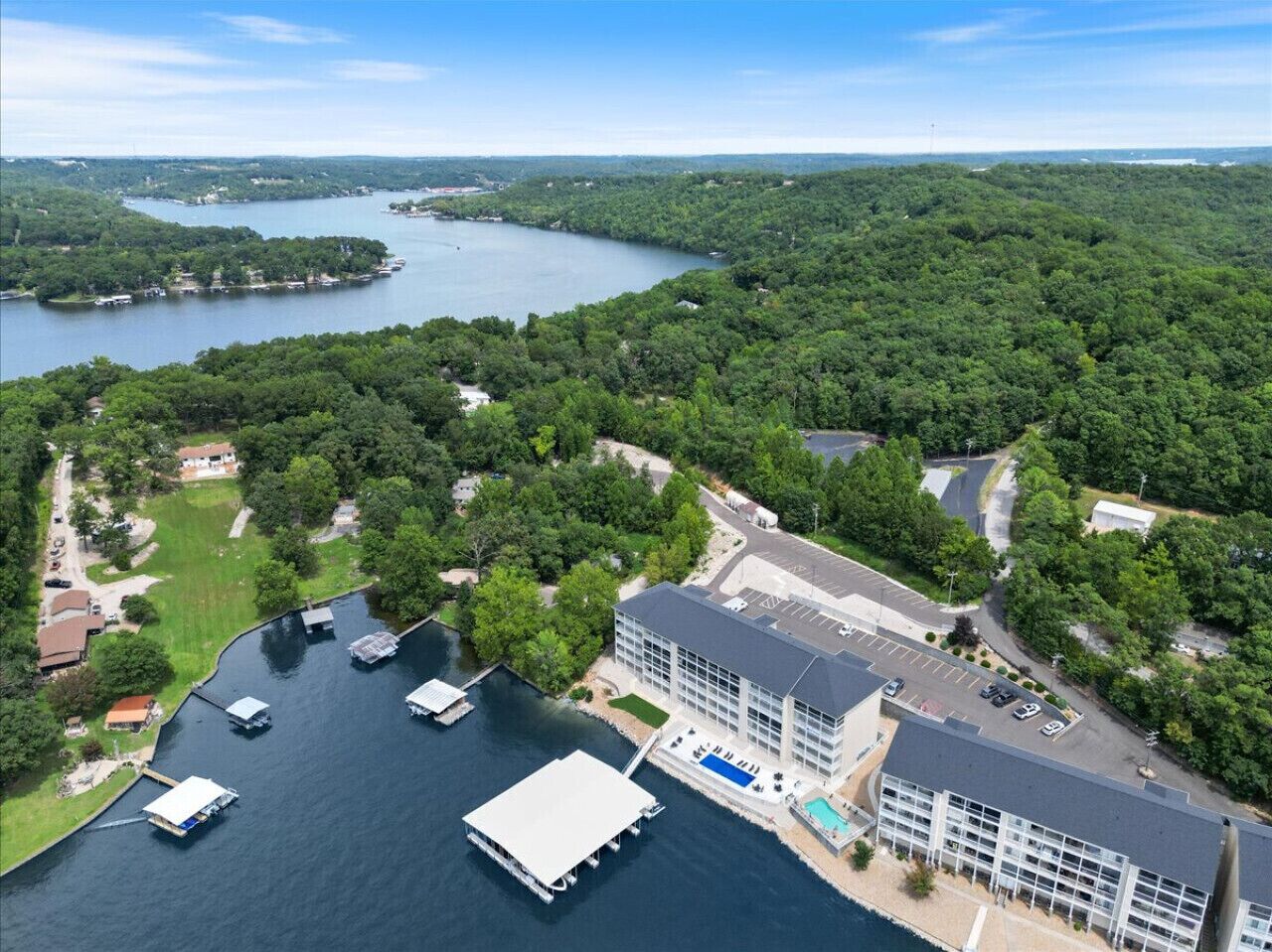 An aerial view of a lakeside property with a large building, docked boats, and surrounding greenery.