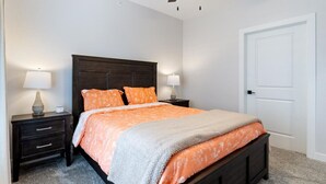 A bedroom with a dark wooden headboard, two bedside tables with lamps, a bed with an orange and grey bedspread, and a white door. - Sierra Bay Sweet Retreat - Two Pools & More! (Camdenton)