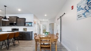 A modern kitchen with dark cabinets, a microwave, and a dining area with a wooden table and chairs. - Sierra Bay Sweet Retreat - Two Pools & More! (Camdenton)