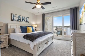 A bedroom with a bed, nightstands, a dresser, a ceiling fan, and a view of a balcony with a grill.
