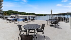 A rooftop pool area with lounge chairs and tables, a swimming pool, and a view of a body of water and hills in the background. - Sierra Bay Sweet Retreat - Two Pools & More! (Camdenton)