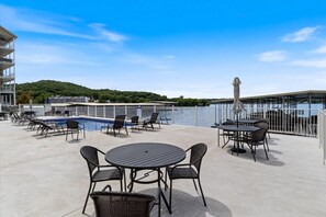 A rooftop pool area with lounge chairs and tables, a swimming pool, and a view of a body of water and hills in the background. - Sierra Bay Sweet Retreat - Two Pools & More! (Camdenton)