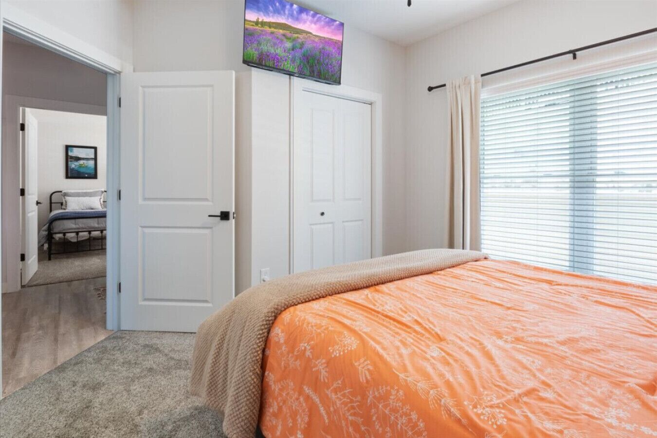 A bedroom with a bed, a wardrobe, a television, and a window with blinds.