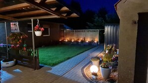 Hyvin valaistu terassialue, jossa on puinen pergola, vihreä nurmikko ja ruukkukasveja.