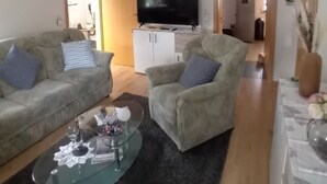 Olohuoneessa on sohva, nojatuoli ja lasinen sohvapöytä. Seinälle on asennettu litteänäyttöinen televisio.