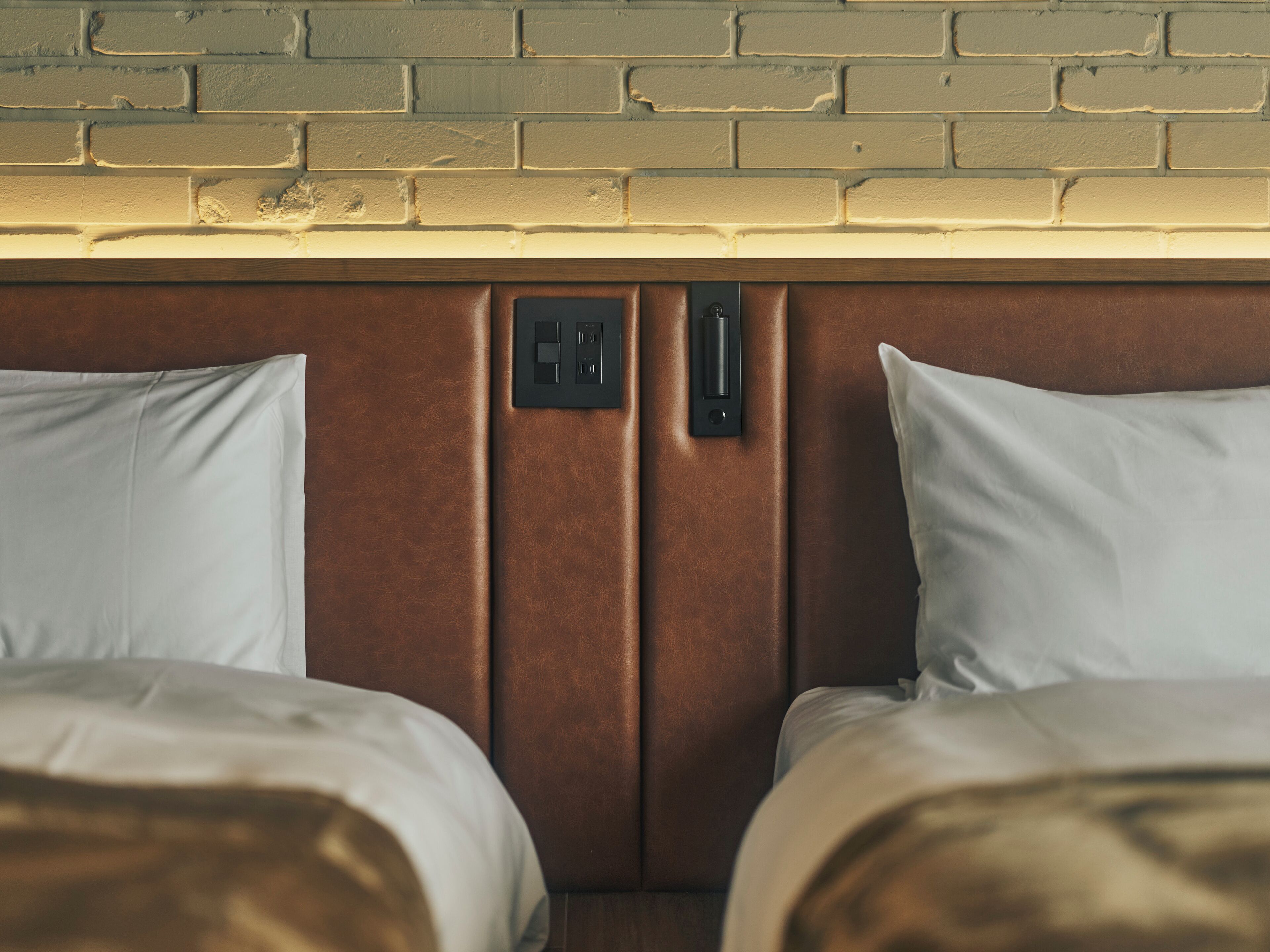 A hotel room with two beds, a brick wall, and a light fixture above the beds.