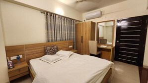 Une chambre à coucher comprenant un lit, des tables de chevet, une armoire, un bureau avec une chaise et une porte.