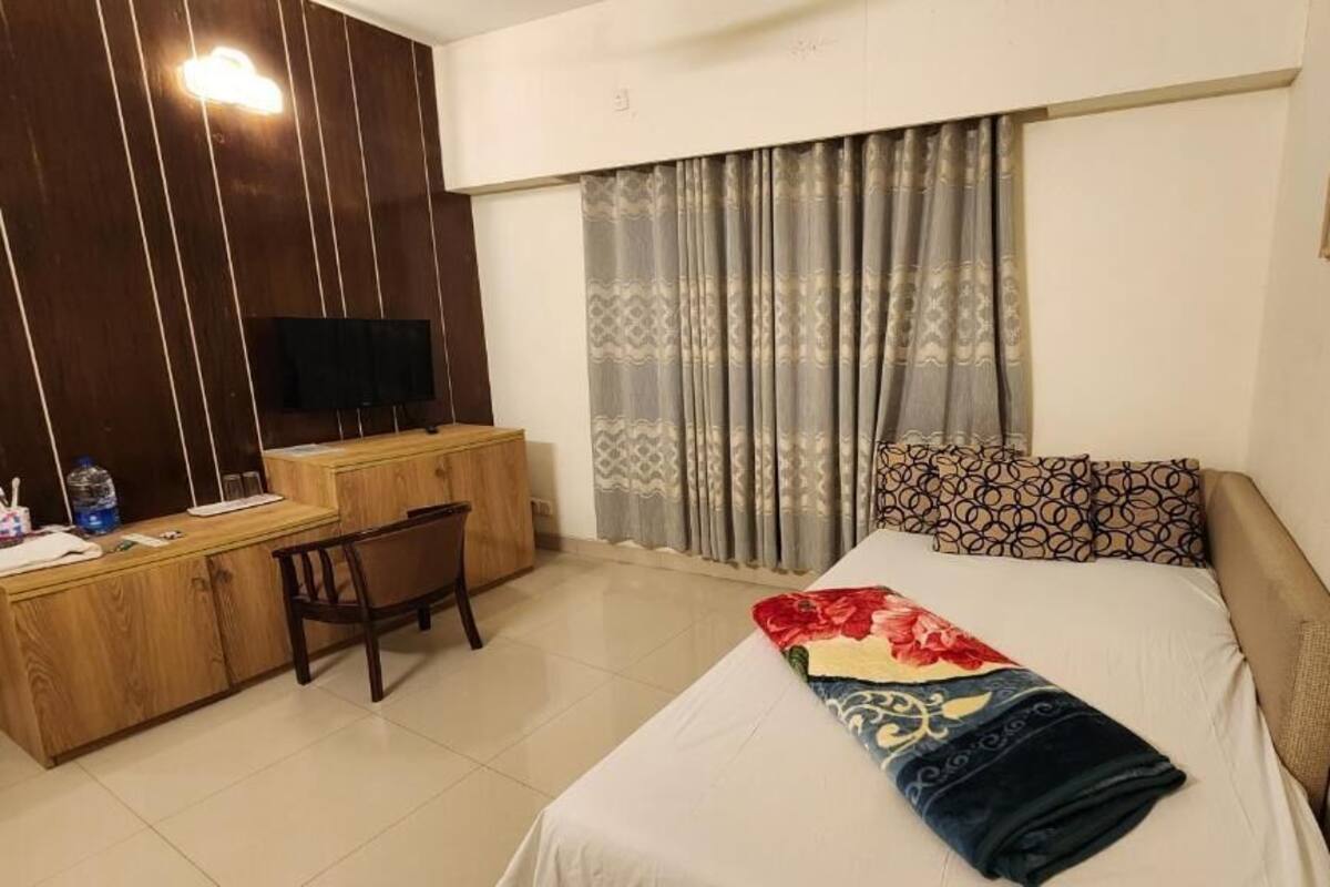 Une chambre d’hôtel avec un lit, un bureau, une chaise, une télévision et des rideaux.