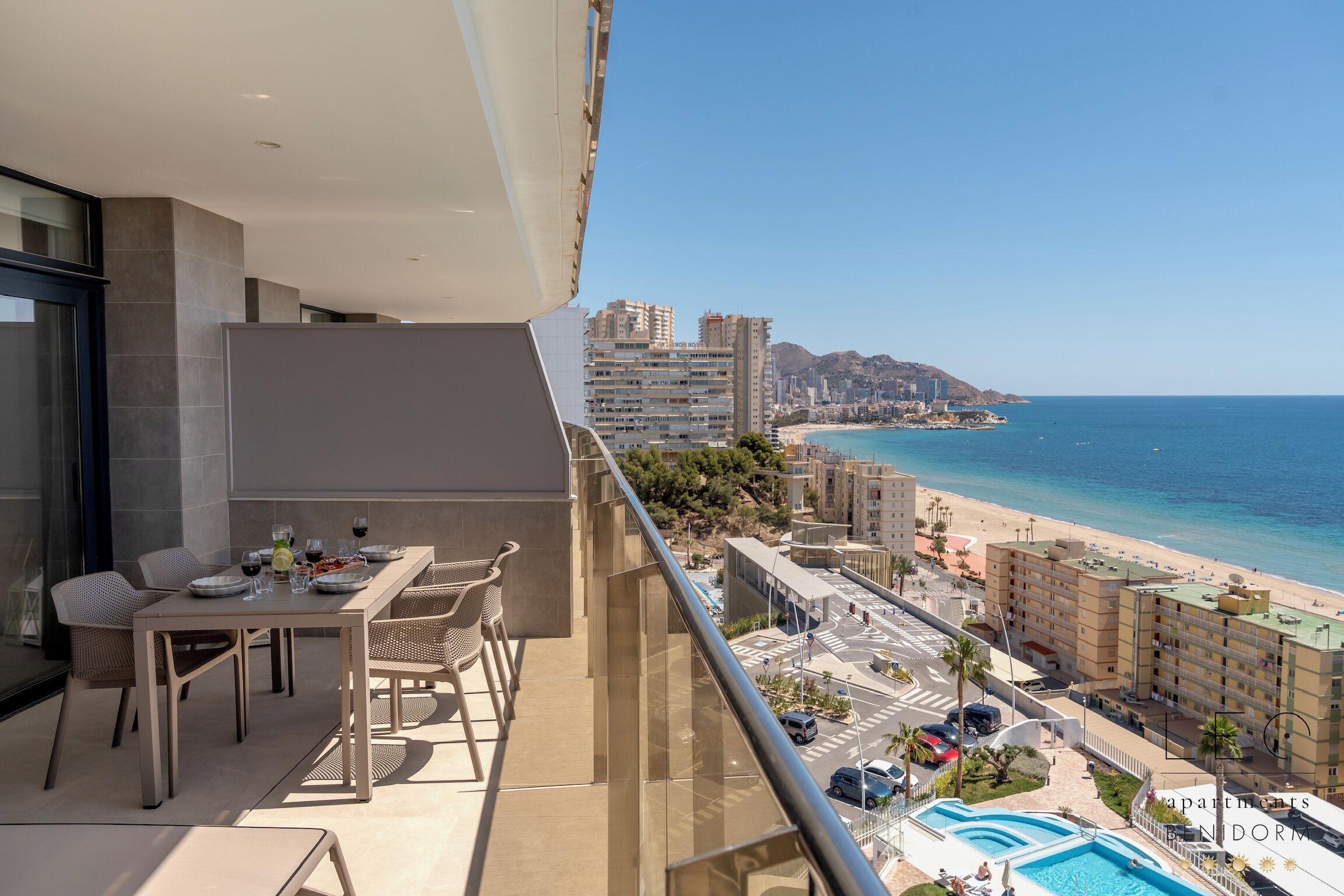 A balcony with a dining table and chairs, overlooking a beach and ocean.