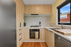 A compact kitchen with wooden cabinets, a built-in oven, and a stainless steel dishwasher.