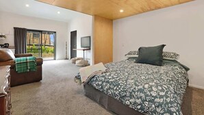 A modern bedroom with a large bed, a sofa, and a TV. - Sundrenched 70's - Spa Pool + Sleep-out, Sleeps 11 (Rotorua)