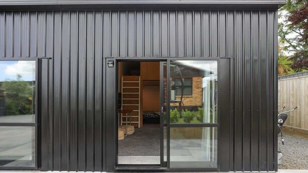 A modern building with a dark exterior and a glass door entrance. - Sundrenched 70's - Spa Pool + Sleep-out, Sleeps 11 (Rotorua)