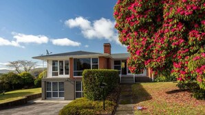 A two-story house with a garage, a covered porch, and a well-maintained lawn. - All Seasons Escape - Hilltop, Sleeps 10, Bikes (Rotorua)