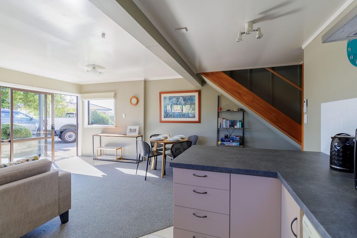 A modern kitchen with a built-in island, a dining area with a table and chairs, and a staircase leading to an upper level.