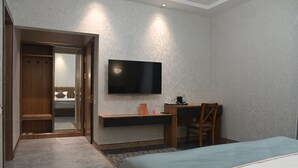 Habitación de hotel con cama, escritorio, silla, televisor y armario.