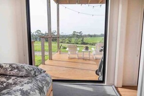 A bedroom with a large window, wooden deck, and outdoor seating area. - Amaroo (Timboon)