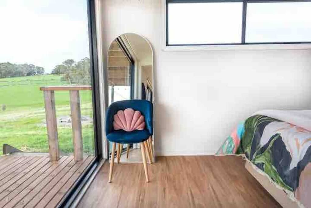 Een kamer met een groot raam, een houten terras, een blauwe stoel en een bed met een kleurrijk sprei.