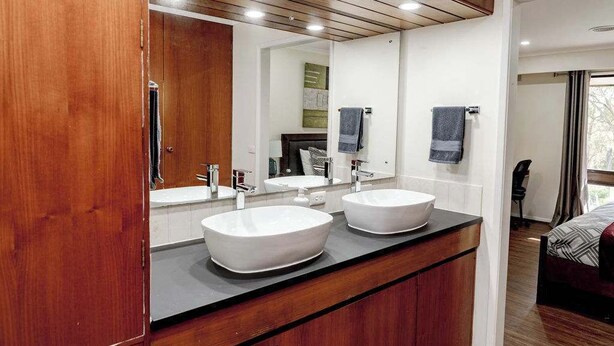 A modern bathroom with two white sinks, a wooden vanity, and a large mirror.