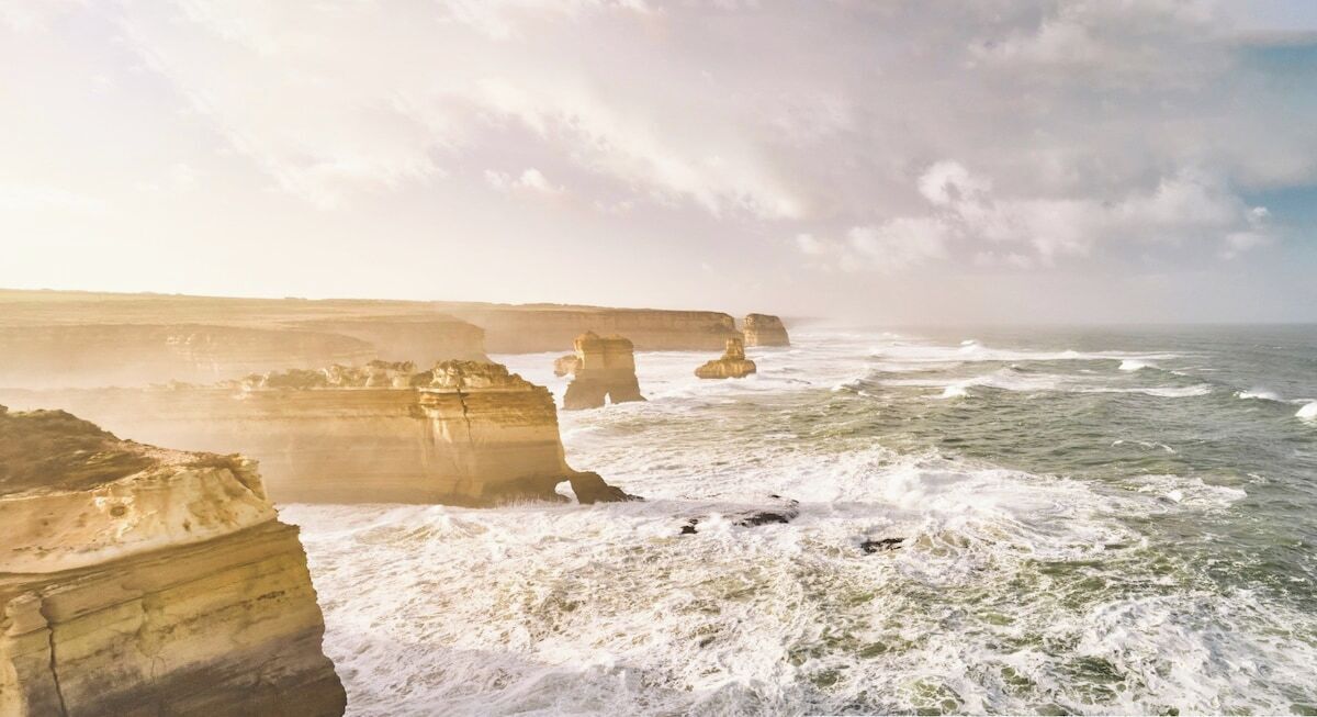 A coastal landscape with large rock formations and waves crashing against them.