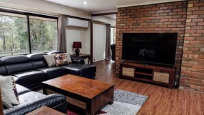 A modern living room with a leather sofa, a wooden coffee table, a flat-screen TV, and a brick fireplace.
