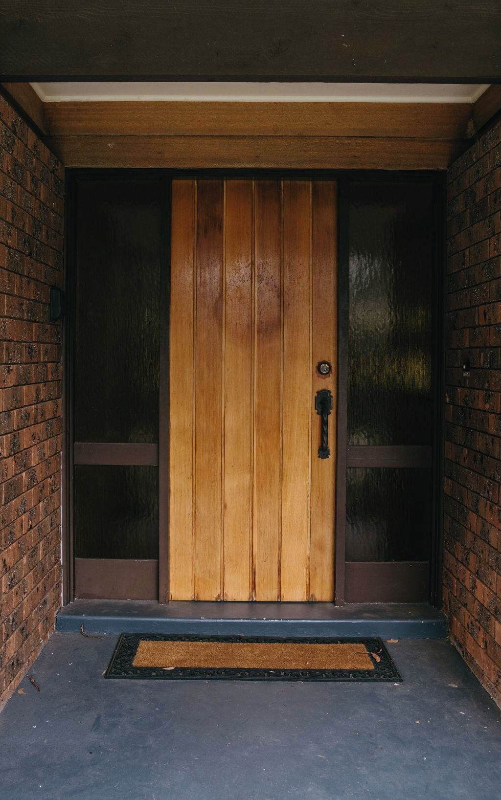 Una porta de fusta amb una mirallera, emmarcada per panells de vidre i un estri de porta al terra.