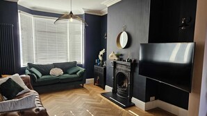 A living room with a dark blue wall, a fireplace, a sofa, a leather armchair, and a television. - Home Away from Home (Coventry)