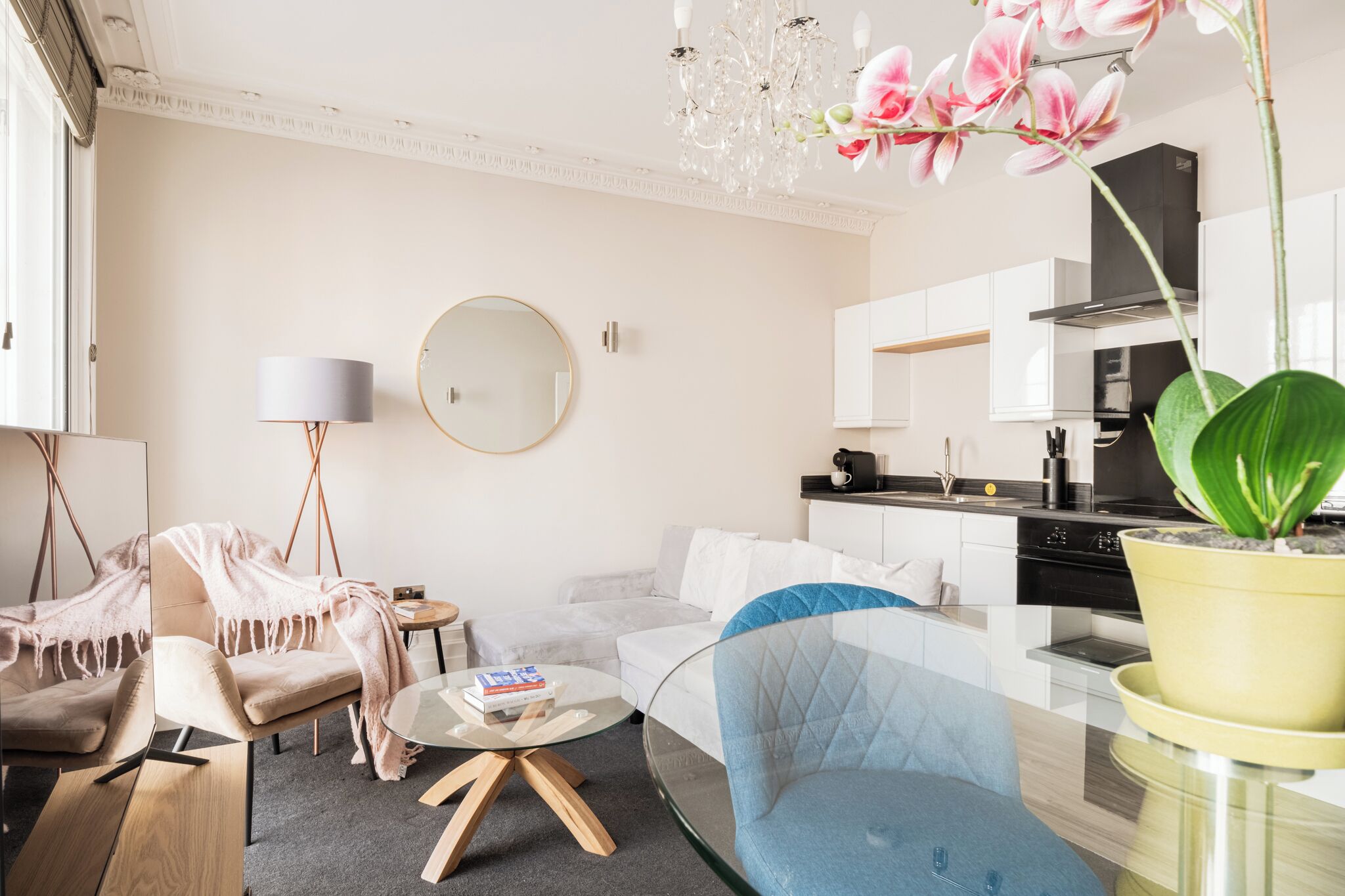 A modern living room with a sofa, a glass coffee table, a round mirror, and a chandelier.