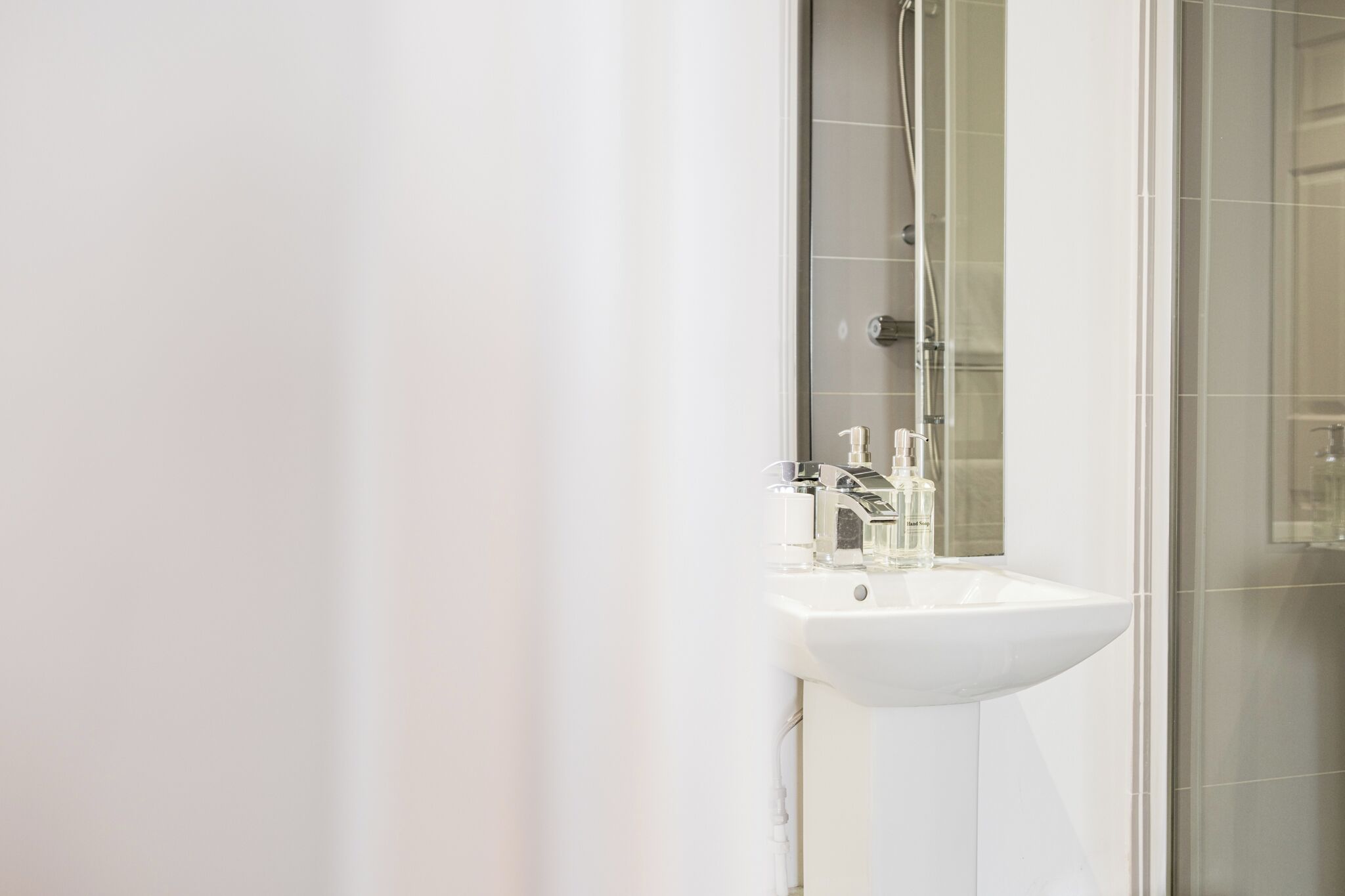 Ein Badezimmer mit einem weißen Waschbecken, einem Spiegel und einer Duschkabine aus Glas.
