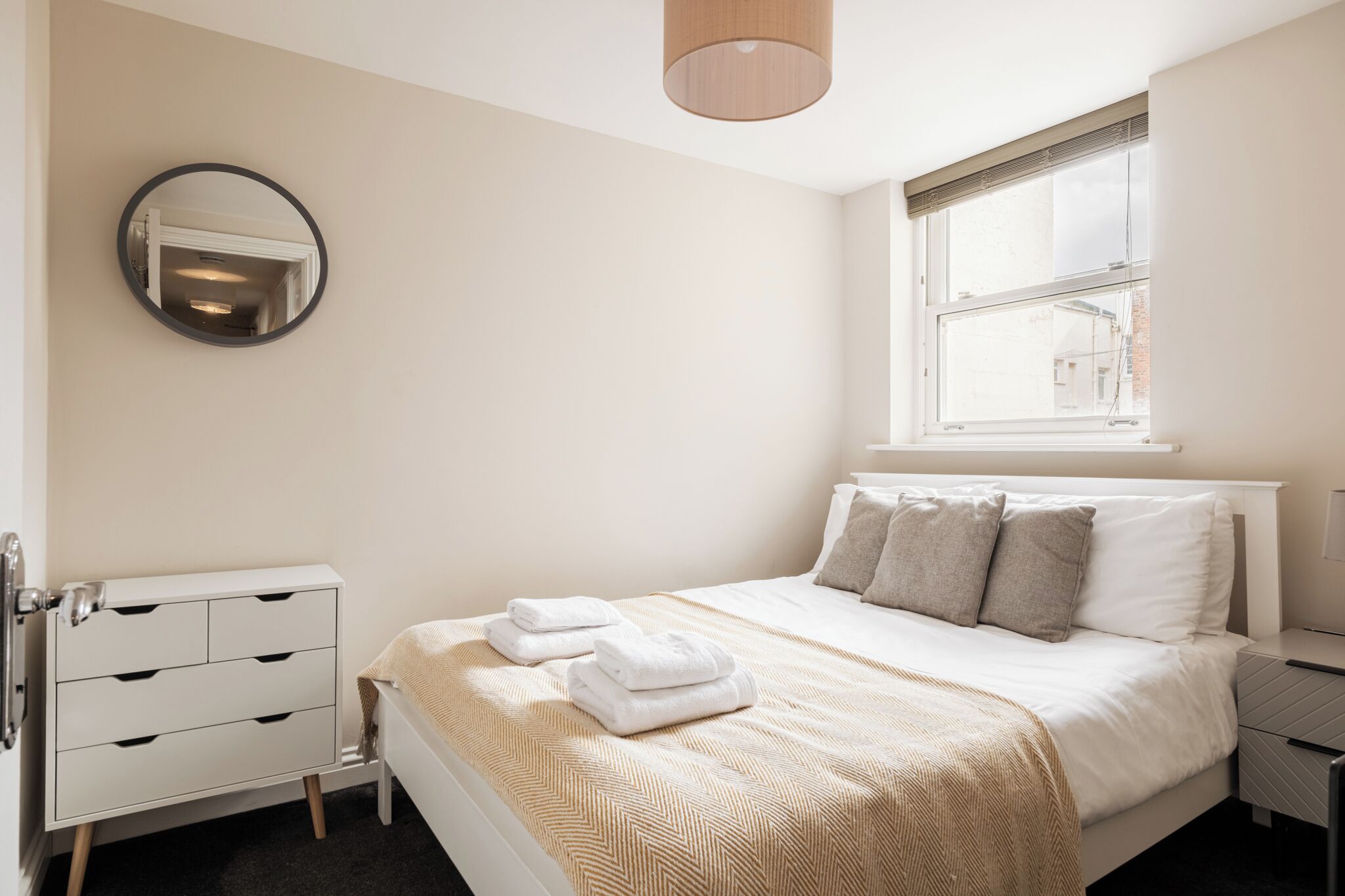 Une chambre à coucher comprenant un lit, une table de chevet, une lampe, une commode, un miroir et une fenêtre.