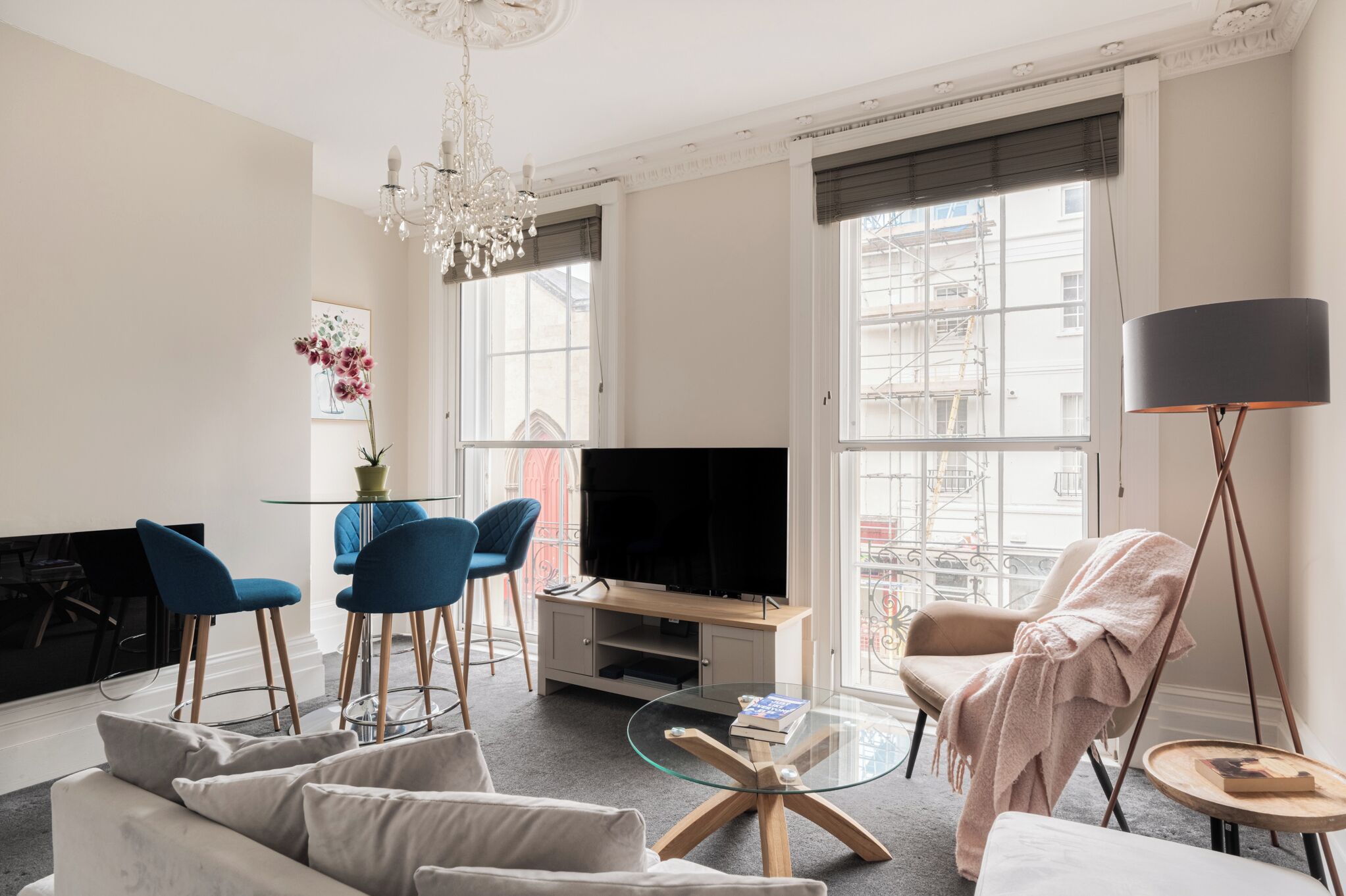 A living room with a TV, blue chairs, a sofa, a glass coffee table, and a chandelier.