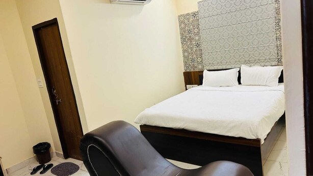 A bedroom with a bed, a chair, a door, and an air conditioning unit.