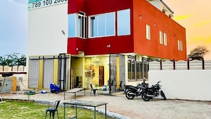 A modern building with a red and white facade, a signboard advertising 'COMFORT IN ROOM RESTAURANT ROOF TOP CAFE GARDEN', and a motorcycle parked in front.