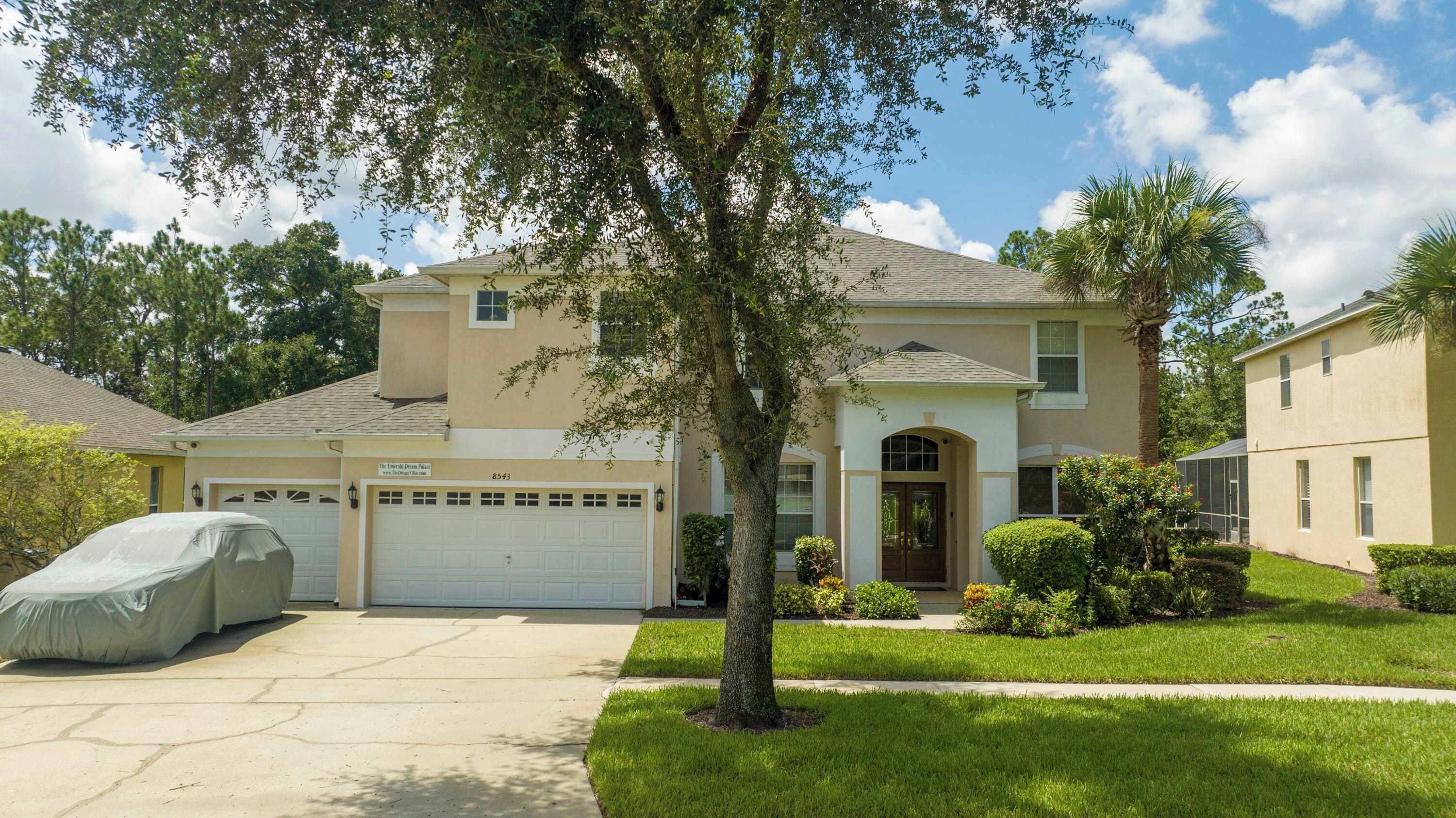 A two-story house with a garage, a covered car, and a well-maintained lawn.