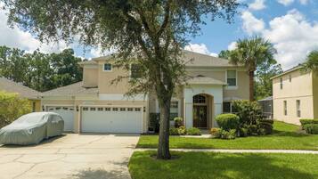 A two-story house with a garage, a covered car, and a well-maintained lawn.