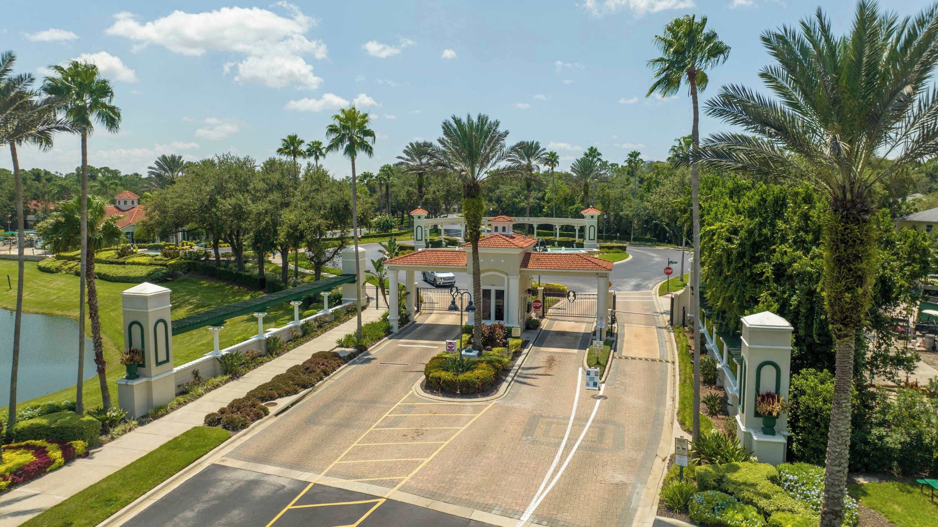 A gated entrance with a covered driveway, palm trees, and a well-maintained lawn.