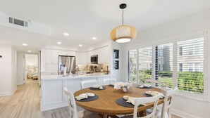Une cuisine moderne avec des meubles blancs, un îlot central et un coin repas comprenant une table ronde et des chaises.